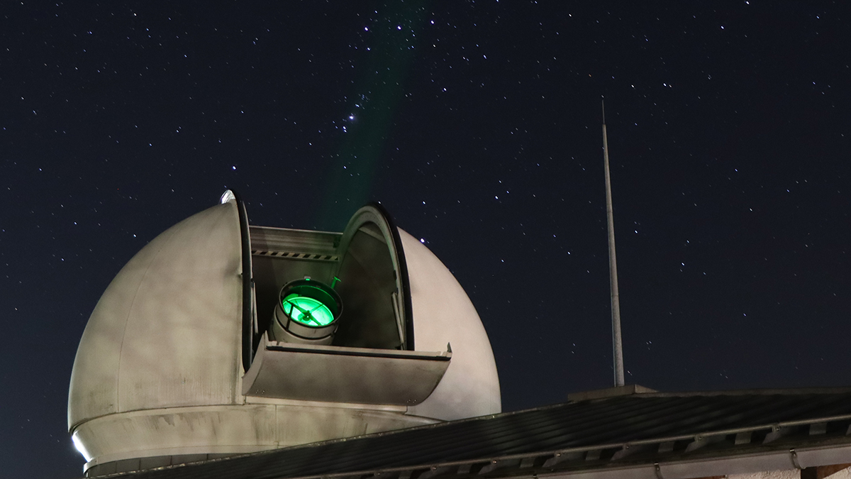 Im Vordergrund eine geöffnete Kuppel des Laser Ranging Systems mit aktivierter Lsereinheit. Im Hintergrund klarer Sternenhimmel. (verweist auf: Abschlussarbeiten am Geodätischen Observatorium Wettzell – ein Erfahrungsbericht)