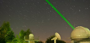 verweist auf: Geodätische Beobachtungsverfahren Bild zeigt eine Satellite Laserranging (SLR) Messstaion mit einem grünen Laserstrahl ins Weltall. (verweist auf: Geodätische Beobachtungsverfahren)